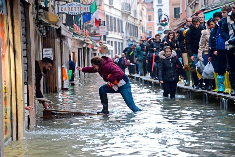 A woman tries to cross a flooded street as people walk on a trestle bridge during high water, in Venice, northern Italy, Nov. 15, 2019.