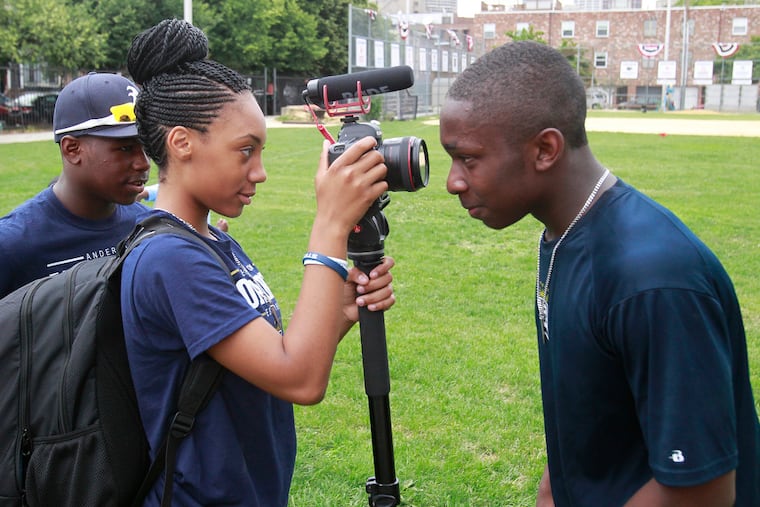 Baseball players Mo'ne Davis (center) and teammate Zaire Witherspoon experiment with a videographer's camera in 2015.