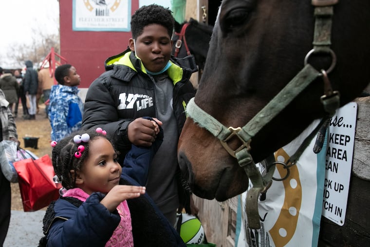 Taleemah Allen, 3, goes to pet a horse next to brother Samir Allen, 14, at the Fletcher Street Urban Riding Club toy giveaway event at their Strawberry Mansion stables in Philadelphia on Saturday, Dec. 18, 2021. Supporters donated more than 500 toys to the famous North Philly horse riding club for the event.