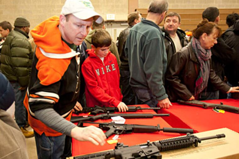 Aubrey Whelen writes about the Philadelphia National Guard Armory Gun Show which opened today in Northeast Philadelphia. Here, Mike Stout reaches for a Mossberg 715T semi automatic 22 rifle as he browes the show with his sons Michael, 11, and Ryan, 23. ( ED HILLE / Staff Photographer )