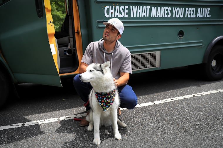 Michael Burlotos pets his dog, Bailey, next to his converted school bus parked in Bellevue State Park in Wilmington, Del on June 1, 2021. Burritos as been traveling the U.S. in the bus with his dog.
