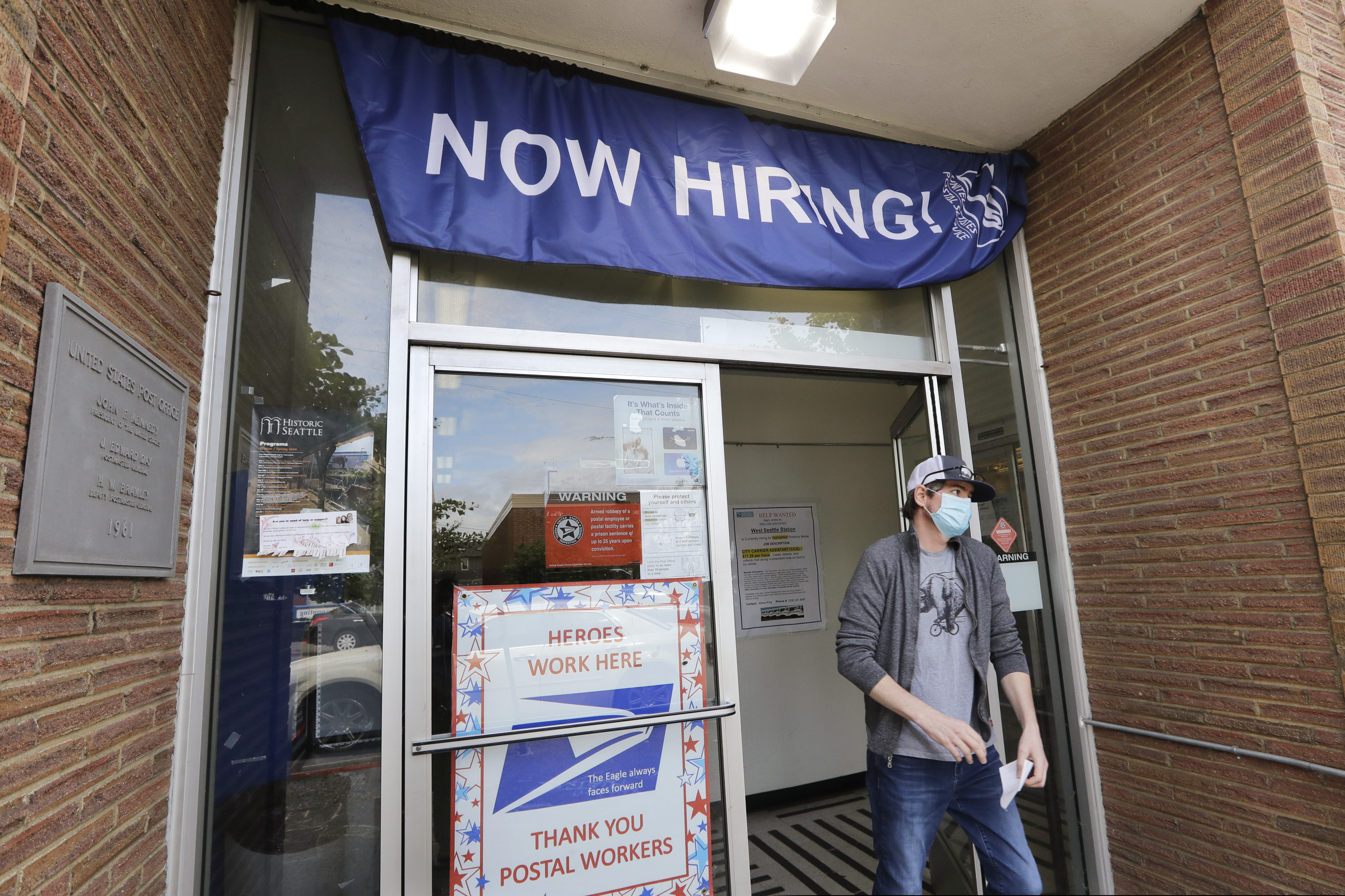 In this June 4 photo, a customer walks out of a U.S. Post Office branch and under a banner advertising a job opening, in Seattle.
