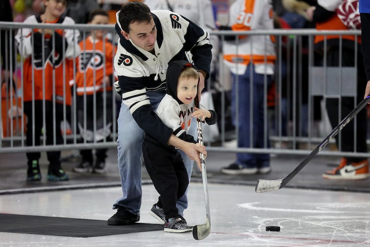 Shawn Paul, 3, gets some help from his father, Zach, as they try the shot-on-goal station at the Flyers Charities Carnival on Sunday.