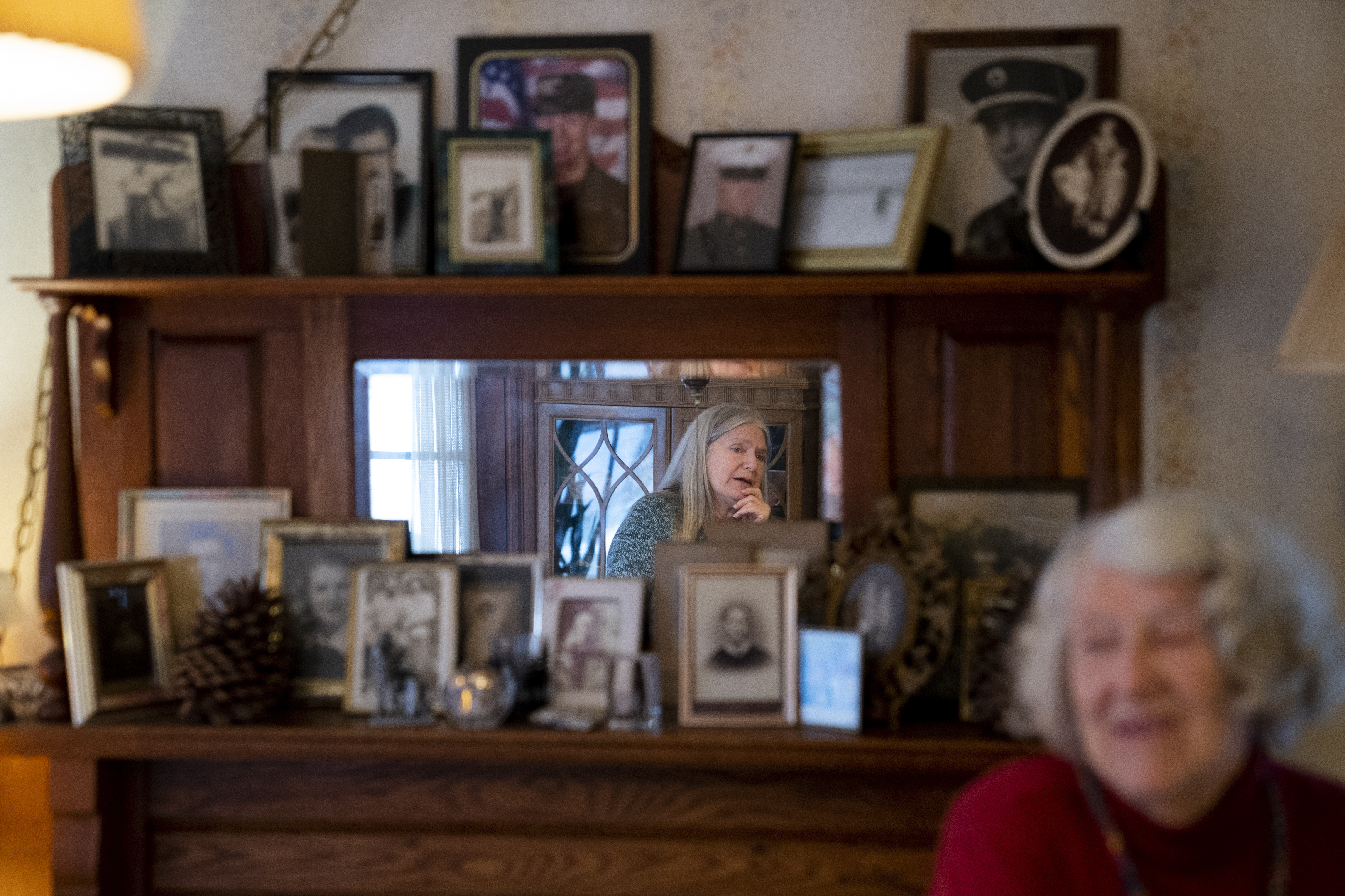 Nancy Rose, center in mirror, speaks with her mother, Amy Russell, right, who both contracted COVID-19 in 2021, in their dining room surrounded by pictures of relatives and family in Port Jefferson, N.Y.