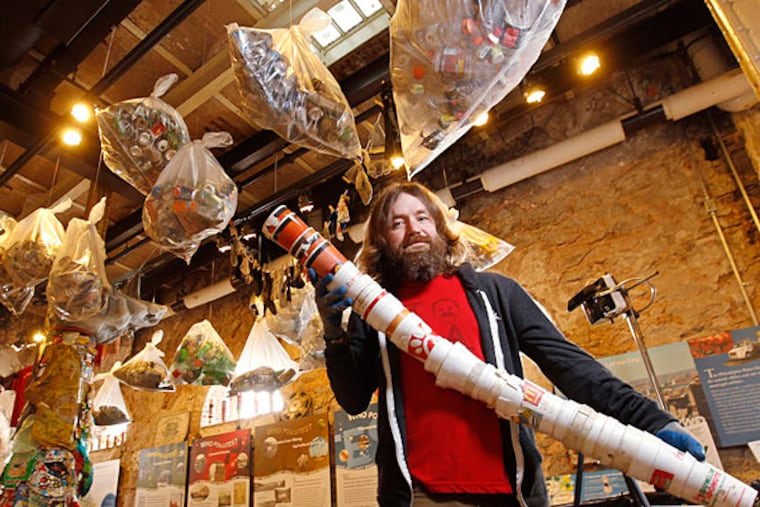 Brad Maule holds up a bunch of styrofoam cups he collected last year in Fairmount Park, with clear bags of trash hanging from the ceiling of the exhibit. Brad Maule , a local writer/artist/environmentalist's mission to clean up Wissahickon Park and make art has reached completion. (Michael Bryant / Staff Photographer )