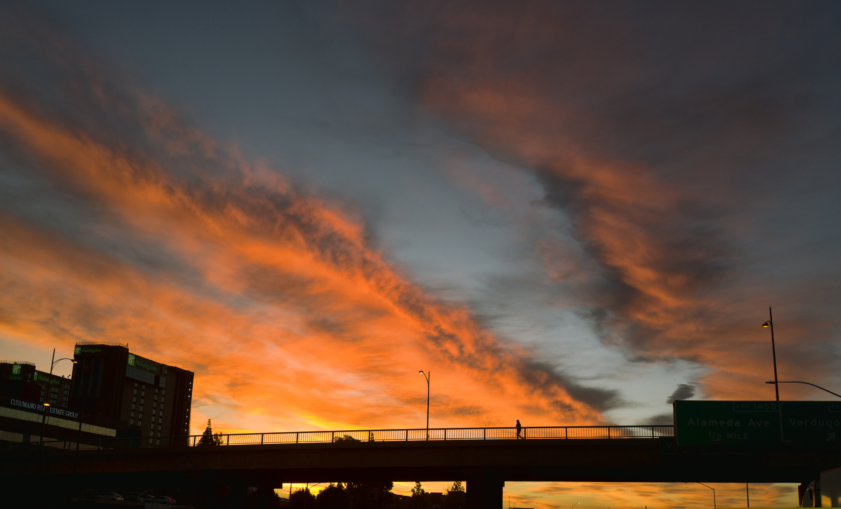 A pedestrian crosses an overpass under a dramatic sunrise during the early morning commute in Los Angeles on Friday, Feb. 1, 2019. A powerful storm heading toward California is expected to produce heavy rainfall, damaging winds, localized stream flooding, and heavy snow in the Sierra Nevada. Forecasters say rain will arrive in the north late Friday afternoon and reach the south late in the night, and last through Saturday night.