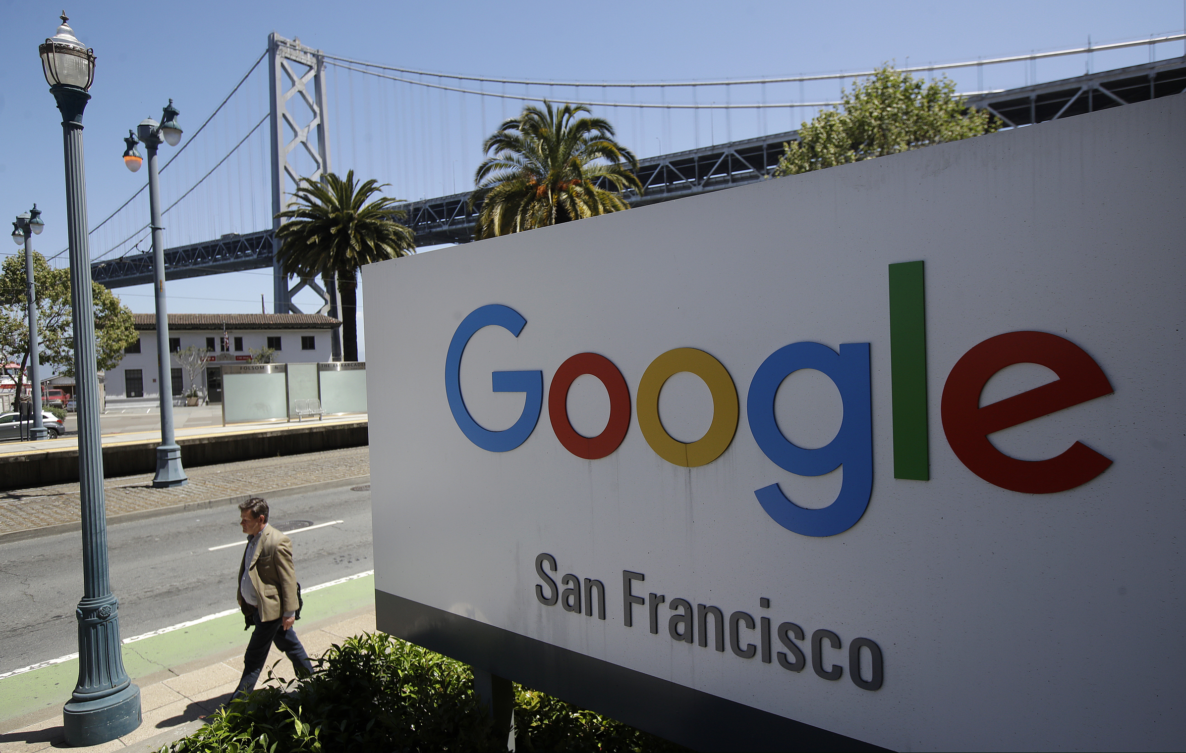 In this May 1, 2019 photo, a man walks past a Google sign outside with a span of the Bay Bridge at rear in San Francisco. Over 90 percent of web searches involve a Google platform, so small businesses have to go through the online giant to get noticed. (AP Photo/Jeff Chiu, File)
