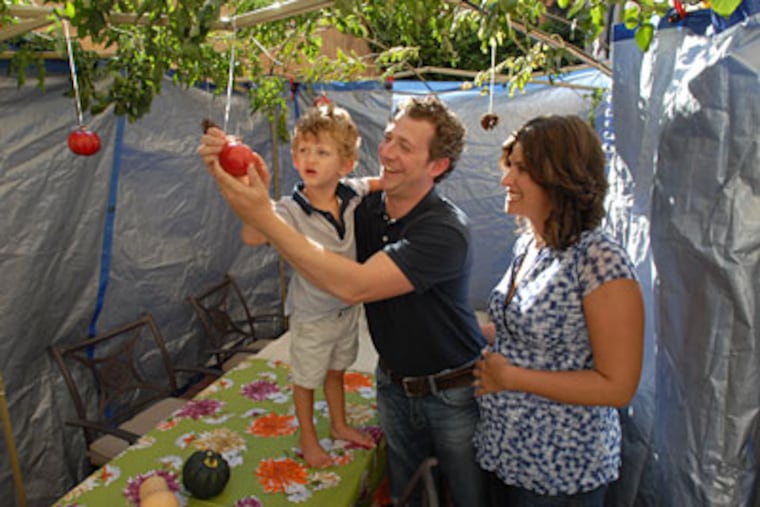 Asher and Sarah Kahn with son Tal in their Queen Village sukkah. Stuffed peppers are a favorite. (APRIL SAUL / Staff Photographer)