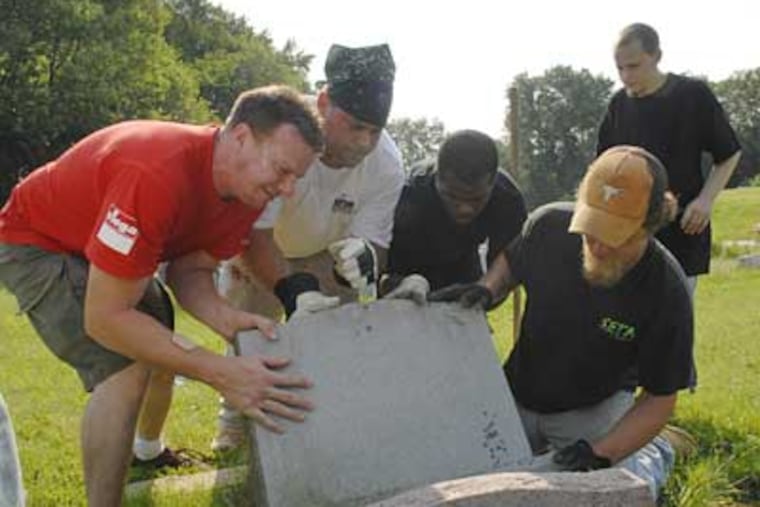 Mike Molinario, above, scrapes caulk off a repaired gravestone at the Harriet Tubman section of Eden Cemetery in Collingdale, where 201 gravestones were knocked over. At left, helpers (from left) Andrew O'Brien, Paul Kernon, Neal Day, and Tom Albany right a gravestone while Tom Weigand watches.