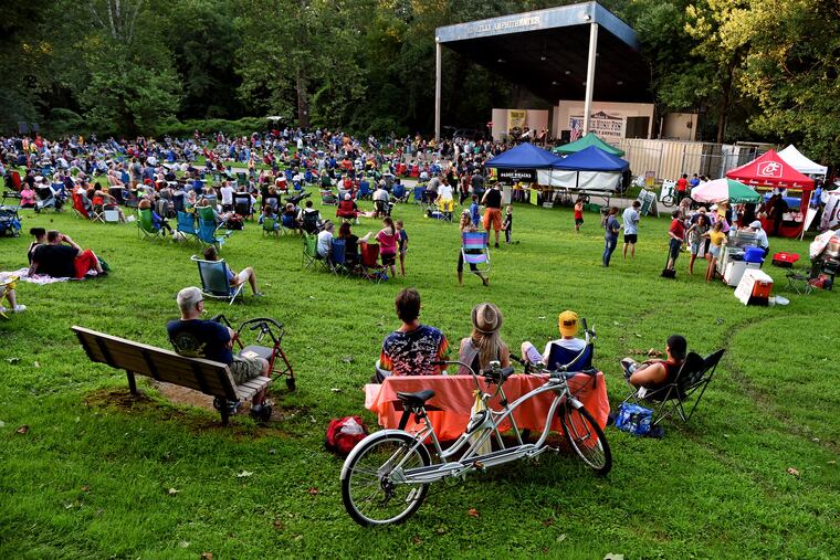 Northeast Philadelphia music lovers Ed Rehl (left), 60; and Janet Heiser (left), 56; sit in front of the vintage Schwinn tandem bicycle they rode to the summer Wednesday night Pennypack Park Music Festival free concert July 24, 2019, where Starman, a tribute band playing the music of David Bowie performs on the Ed Kelly Amphitheater stage. Heiser came to concerts there in the 1980s with her mother when her children were toddlers. "It was big bands in those days, and we even had Al Alberts play here." (Alberts was a Philadelphia music star. He formed the Four Aces in the 1950s, and later recorded "On the Way to Cape May," still a Jersey Shore classic. Even later he hosted a Saturday afternoon talent TV show for youngsters called Al Alberts Showcase.