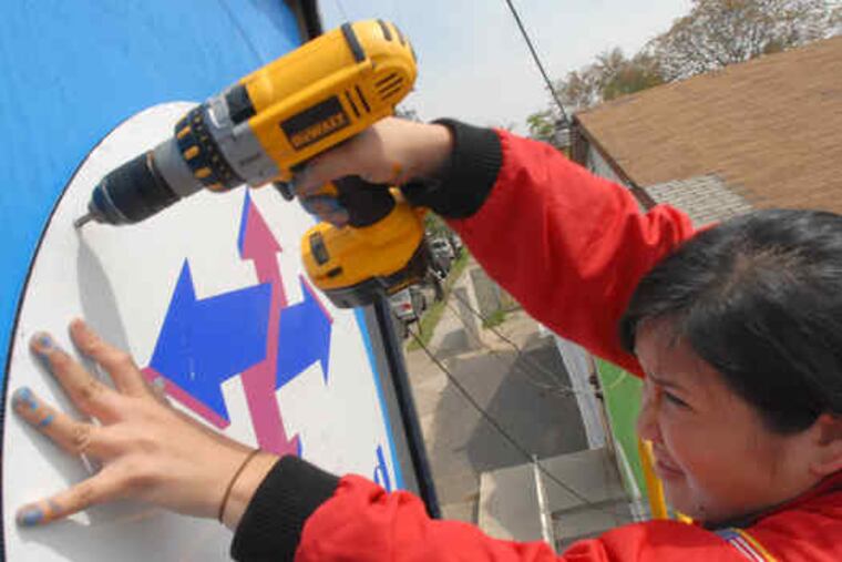 Dorothy Wong hangs a sign for the day-care center, to be run by Respond, a nonprofit, where the sign for the old Holmes Lounge hung. One hundred volunteers gathered to work on the project.