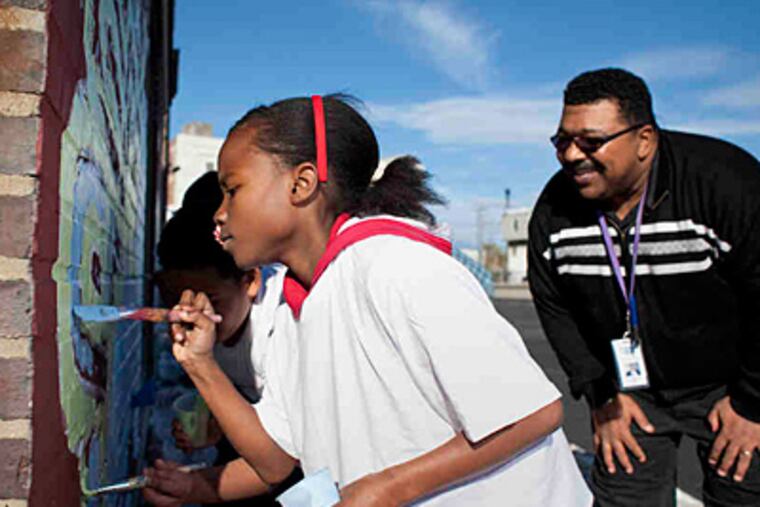 Roxanne Josey, 10, a fifth grader at Blankenburg Elementary School, carefully paints a portion of the mural under the watchful eye of Charles Graham, parent and community ombudsman. (Ed Hille/Staff)