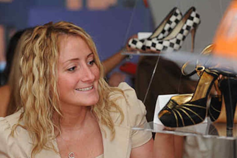 Liz Johnson of Mays Landing checks out Stephanie LaGrossa's size 7's at last week's auction, which raised money for women battling cancer. (Bob Williams / For the Inquirer)