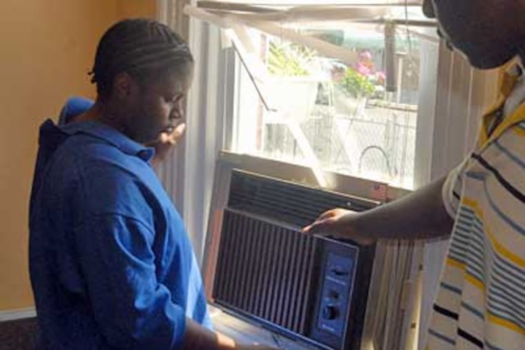 Shamika and Dan King install a donated air conditioner in a living-room window. (Ron Tarver/Inquirer)