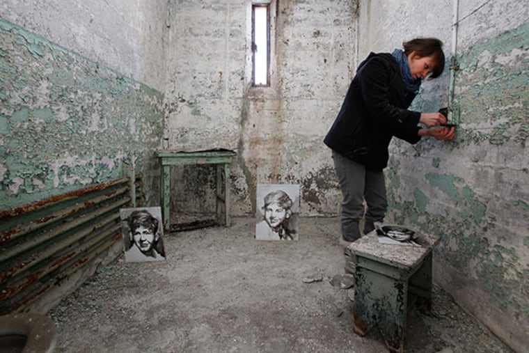 Artist Cindy Stockton Moore tightens a monfilament that holds test works in a cell that have been hanging up since November at Eastern State Penitentiary, January 29, 2014. She will be showing ink pen on mylar portraits of victims killed by inmates in an exhbit scheduled for May. ( MICHAEL S. WIRTZ / Staff Photographer )