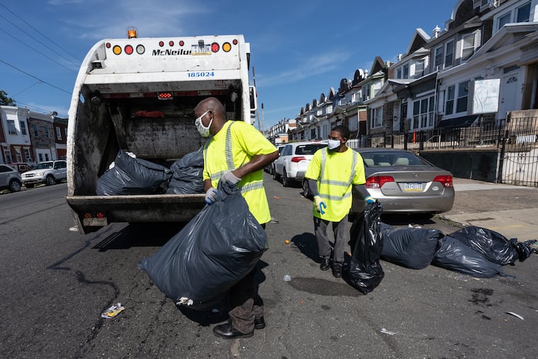 Sanitation workers Lawrence Brown, left, and Rashan Purcell, right, collect trash on East Allegheny Ave., in Philadelphia July 27, 2020.