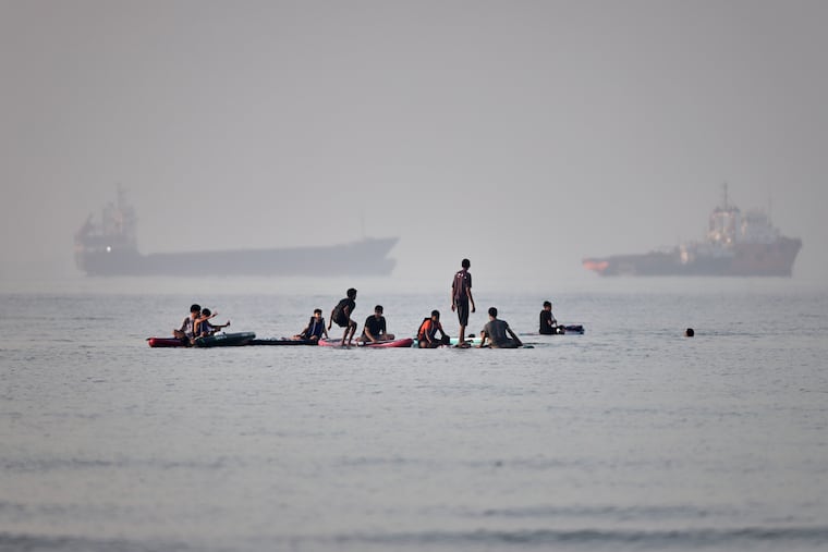 People gather on paddleboards in shallow water as cargo and service vessels are anchored in the Strait of Hormuz off Bandar Abbas, Iran, Monday, June 1, 2026.