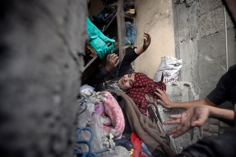 Palestinians try to rescue a woman stuck under the rubble of a destroyed building following Israeli airstrikes in Khan Younis refugee camp, southern Gaza Strip, on Thursday, Dec. 7, 2023.