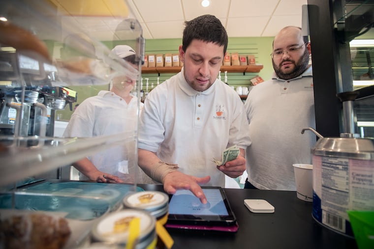 Eric Cohen, center, rings up a customer while manager Jonathan Dorfman, right, stands ready to help at the New Avenue Cafe in Havertown, PA on October 21, 2019. The New Avenue Cafe operates inside the Kelly Center and employees special-needs adults.