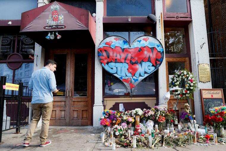 A pedestrian passes a makeshift memorial for the slain and injured victims of a mass shooting that occurred in the Oregon District early Sunday morning, Wednesday, Aug. 7, 2019, in Dayton, Ohio. President Donald Trump is headed to Dayton and El Paso, Texas on Wednesday to offer a message of healing and unity, but he will be met by unusual hostility in both places by people who fault his own incendiary words as a contributing cause to the mass shootings . (AP Photo/John Minchillo)