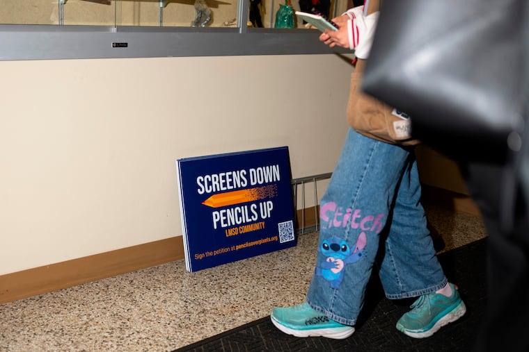 Signs reading, "Screens down, pencils up" at a Lower Merion School District meeting. Seven families are suing the school district over its repeal of a policy that allowed families to opt-out of computer usage.