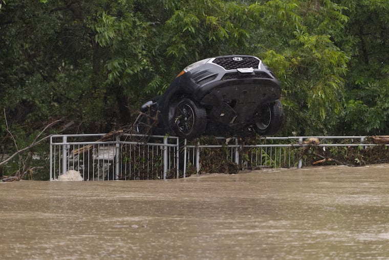 A flood-damaged car hangs from a fence Wednesday in Boerne, Texas.