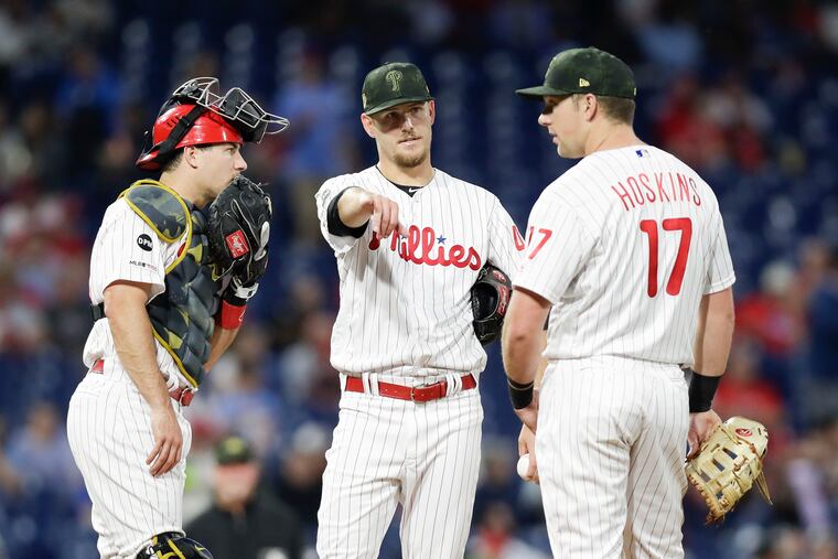 Cole Irvin conferences with J.T. Realmuto (left) and Rhys Hoskins during the Phillies' series against the Rockies.