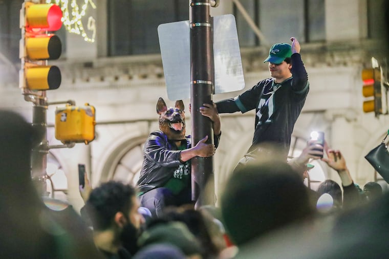 Eagles fans — including one wearing the underdog mask popularized during the team’s last Super Bowl run — climb a pole in Center City after the Eagles advanced to the Super Bowl last month.