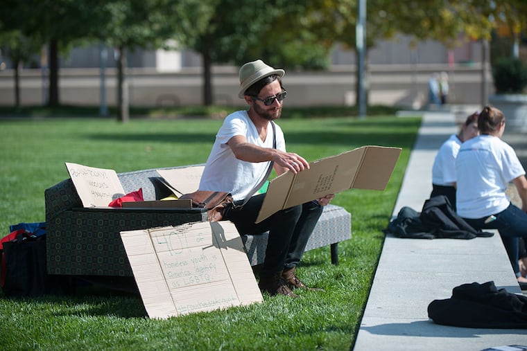 Paul Robertus of Laurel, Mont., reads one of the signs before posing for a photo on Valley Youth House’s conversation-starting couch at the National Constitution Center, one of its stops Thursday. (TRACIE VAN AUKEN/For The Inquirer)