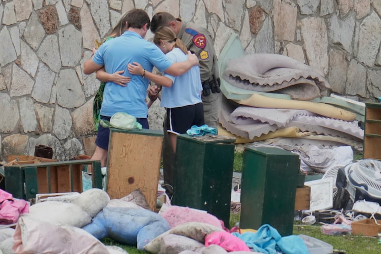 An officer prays with a family as they pick up items at Camp Mystic in Hunt, Texas, on July 9, 2025.