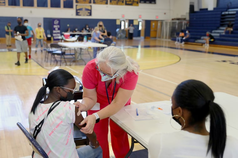 Nurse Kimball Dunlap (center) puts a bandage on the arm of Kimonee Washington, 12, after administering the first dose of the Pfizer COVID-19 vaccine during a clinic for children 12 and older at Cheltenham High School in May.