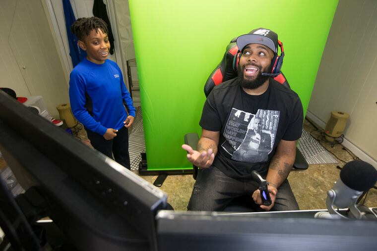 E-sports gamer David Carter of Drexel Hill has about 850,000 followers on YouTube, Facebook, Twitter and Instagram. He does his filming e-sports videos, editing and chatting out of the basement of his Drexel Hill row home. His son David, 11, left, gives him a hard time as he plays in the basement gaming area on April 25, 2019.