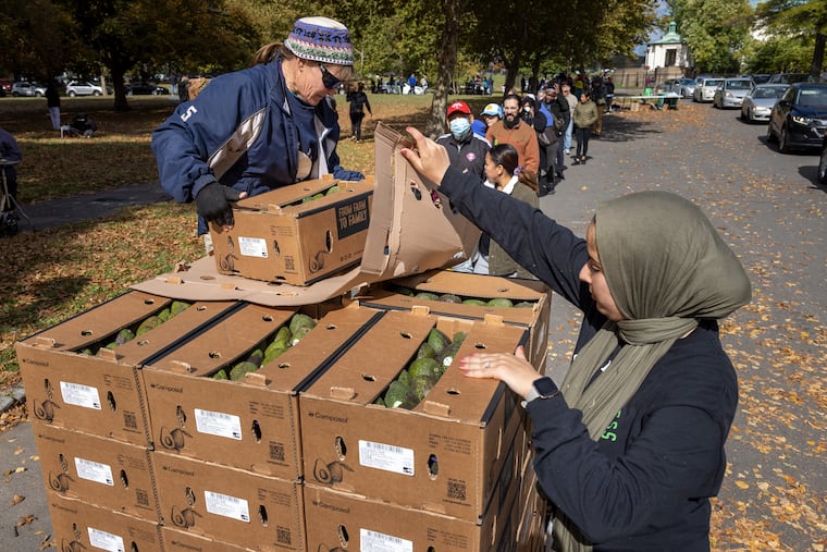 Volunteer Bobbie Beebe, left, and Nourhan Ibrahim, right, development director with Sharing Excess, organize and distribute boxes of avocados at FDR Park in South Philadelphia.