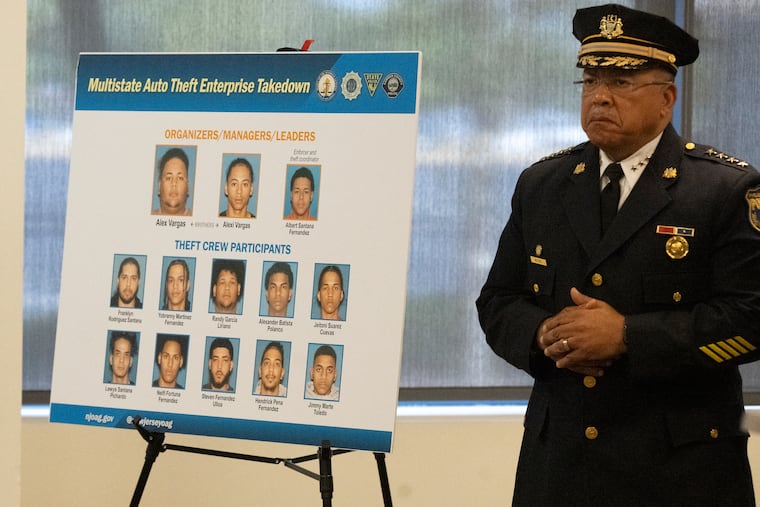 Philadelphia Police Commissioner Kevin J. Bethel stands next to the mugshots of 13 men charged in connection to a South Jersey-based auto theft ring linked to the killing of a Philadelphia police officer.