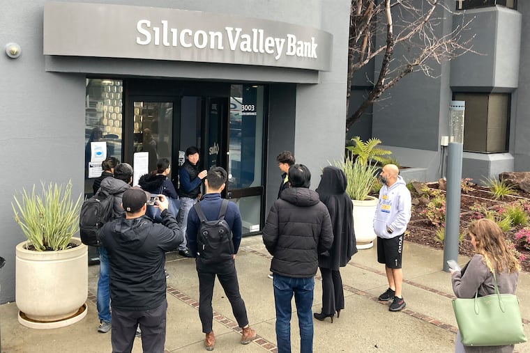 A person from inside Silicon Valley Bank, middle rear, talks to people waiting outside of an entrance to Silicon Valley Bank in Santa Clara, Calif.. The Federal Deposit Insurance Corporation seized the assets of the bank on Friday, marking the largest bank failure since Washington Mutual during the height of the 2008 financial crisis.