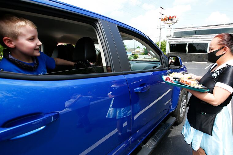 In Thorndale, Chester County, Happy Day's Family Bistro waitress Angeline Vega (right) serves food to customers as Frank Karolczak looks on in the restaurant parking lot on Friday. The bistro offers "carhop" service during the coronavirus pandemic. People drive up, place their order, and get food delivered to their car.