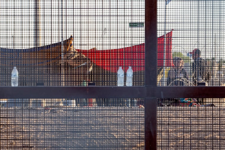 Two migrants, part of a small group, are seeing through the mesh of the border fence as they camp outside a gate in El Paso, Texas, in 2023.