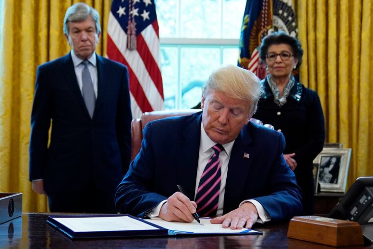 President Donald Trump signs a coronavirus aid package to direct funds to small businesses, hospitals and testing, in the Oval Office of the White House on Friday.