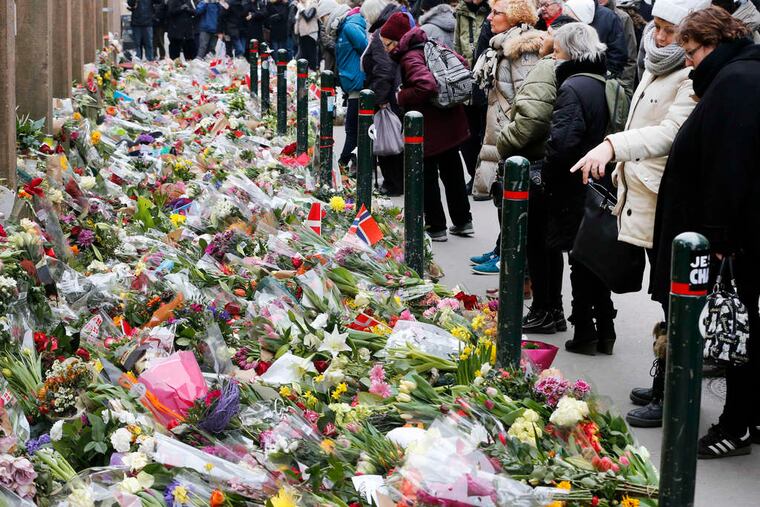People pay their respects before flowers in front of a synagogue in Copenhagen, Denmark, where a gunman killed a volunteer security guard.
