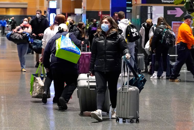 Travelers trek through Terminal E at Logan Airport, Tuesday, Dec. 21, 2021, in Boston. At least three major airlines say they have canceled dozens of flights, Friday, Dec. 24, because illnesses largely tied to the omicron variant of COVID-19 have taken a toll on flight crew numbers during the busy holiday travel season.