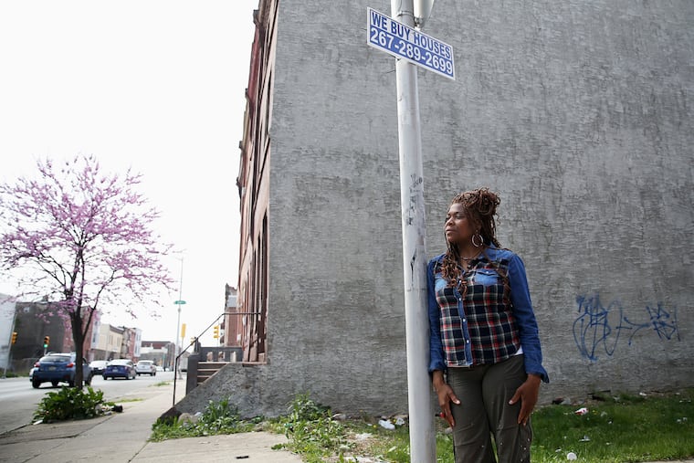 Tonetta Graham, president of the Strawberry Mansion Community Development Corporation, under a "We Buy Houses" sign in Philadelphia's Strawberry Mansion section. Her organization has been urging neighborhood homeowners to be wary of aggressive home purchasing efforts.