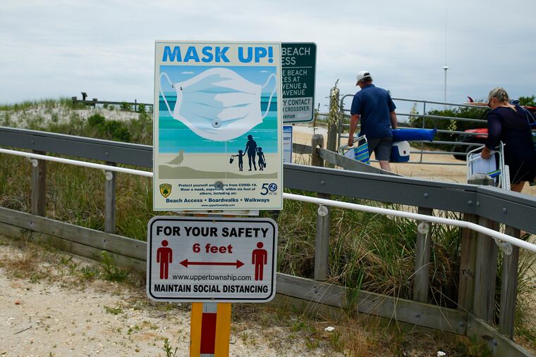 Pedestrians walk to the Strathmere, New Jersey beach past signs instructing beachgoers to wear masks and maintain social distancing on Thursday.