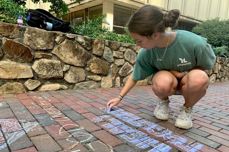 UNC-Chapel Hill sophomore Ashley Tatem writes "Heal Together" on a walking path outside the campus student center in Chapel Hill, N.C., Tuesday, Aug. 29, 2023, the day after a graduate student fatally shot his faculty adviser.