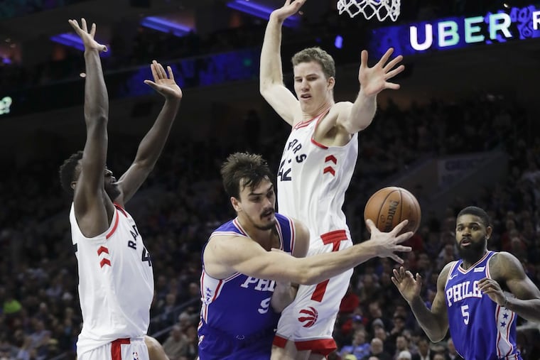 Sixers forward Dario Saric passes the basketball to teammate forward Amir Johnson past Toronto Raptors forward Pascal Siakam (left) and center Jakob Poeltl on Thursday, December 21, 2017 in Philadelphia.