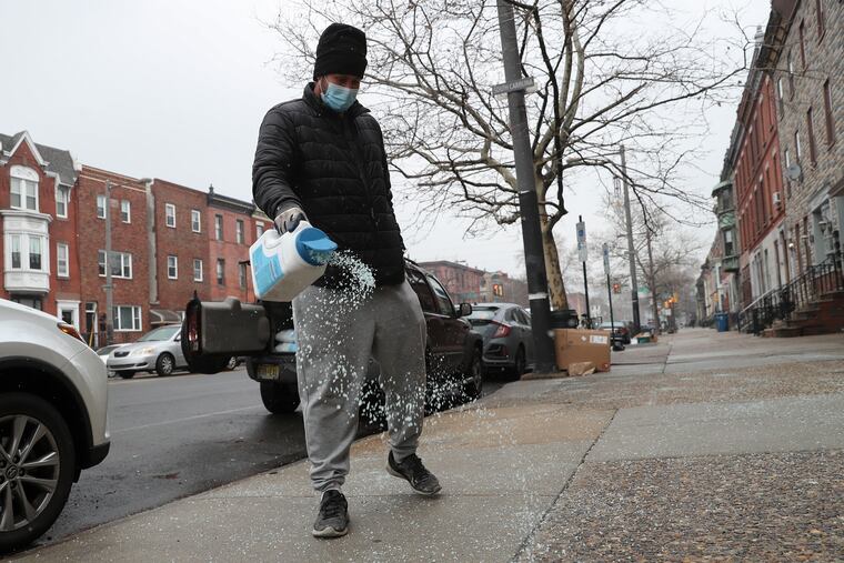 Cleber Alves salts the sidewalk on Broad between Dickinson and Tasker streets in Philadelphia on Friday, Jan. 28, 2022. A major winter storm is expected Friday night into Saturday.