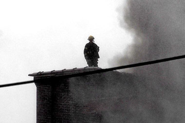 A firefighter works as a spotter, watching flareups from the roof of an adjacent building as the 7-alarm fire is brought under control.