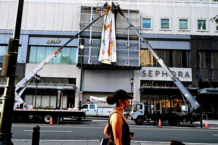 August 1, 2022: Workers change out a large billboard on the facade of Market Street East’s Fashion District Philadelphia.