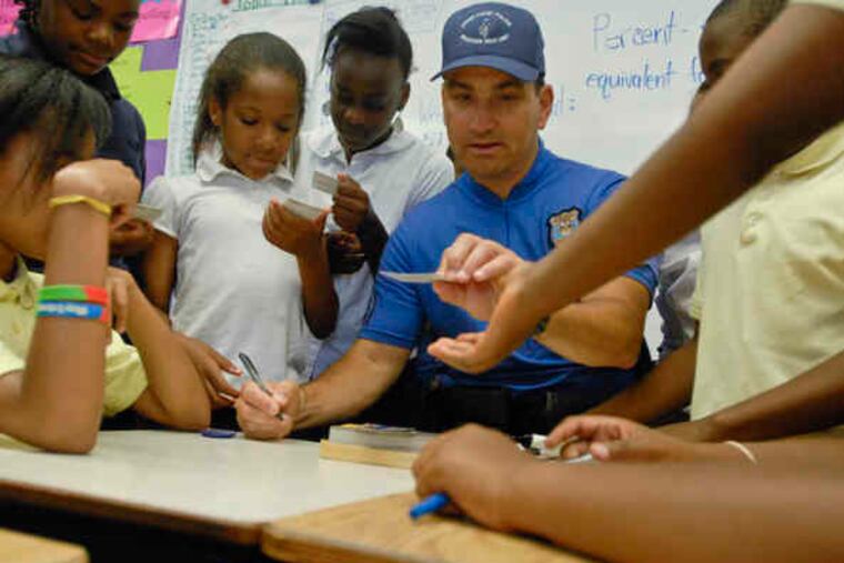 In a monthly visit to Susan Phillips' fifth-grade class at Stonehurst Hills Elementary, Upper Darby Patrolman James Reif signs cards featuring himself. Below, he and student Khalil Sulayman hand-wrestle.
