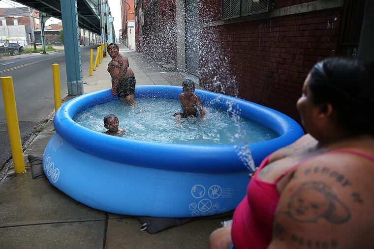 Maria Schermety, left, sprays her grandchildren with water as they play in a pool on the sidewalk along Front Street near Cecil B. Moore Avenue in Philadelphia on July 20, 2015. The children are lIsaiah Pizarro, 3, left, Zahamir Burch, 9, center, and Isaac Adorno, 6, right. ( DAVID MAIALETTI / Staff Photographer )