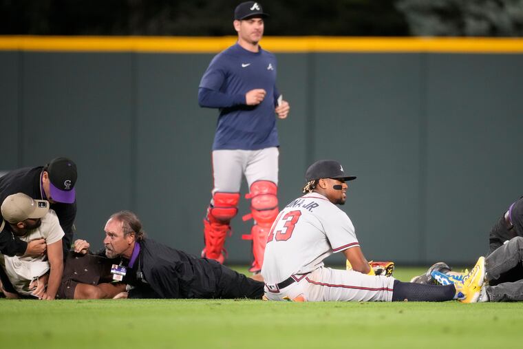 Atlanta Braves right fielder Ronald Acuna Jr. (center) ends up on the turf as field guards wrestle down two fans who approached him as he took his spot in the field for the bottom of the seventh inning against the Colorado Rockies.